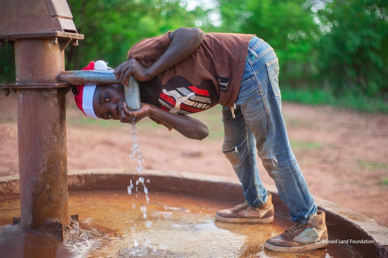 A boy drinking clean water from a borehole in rural Zambia